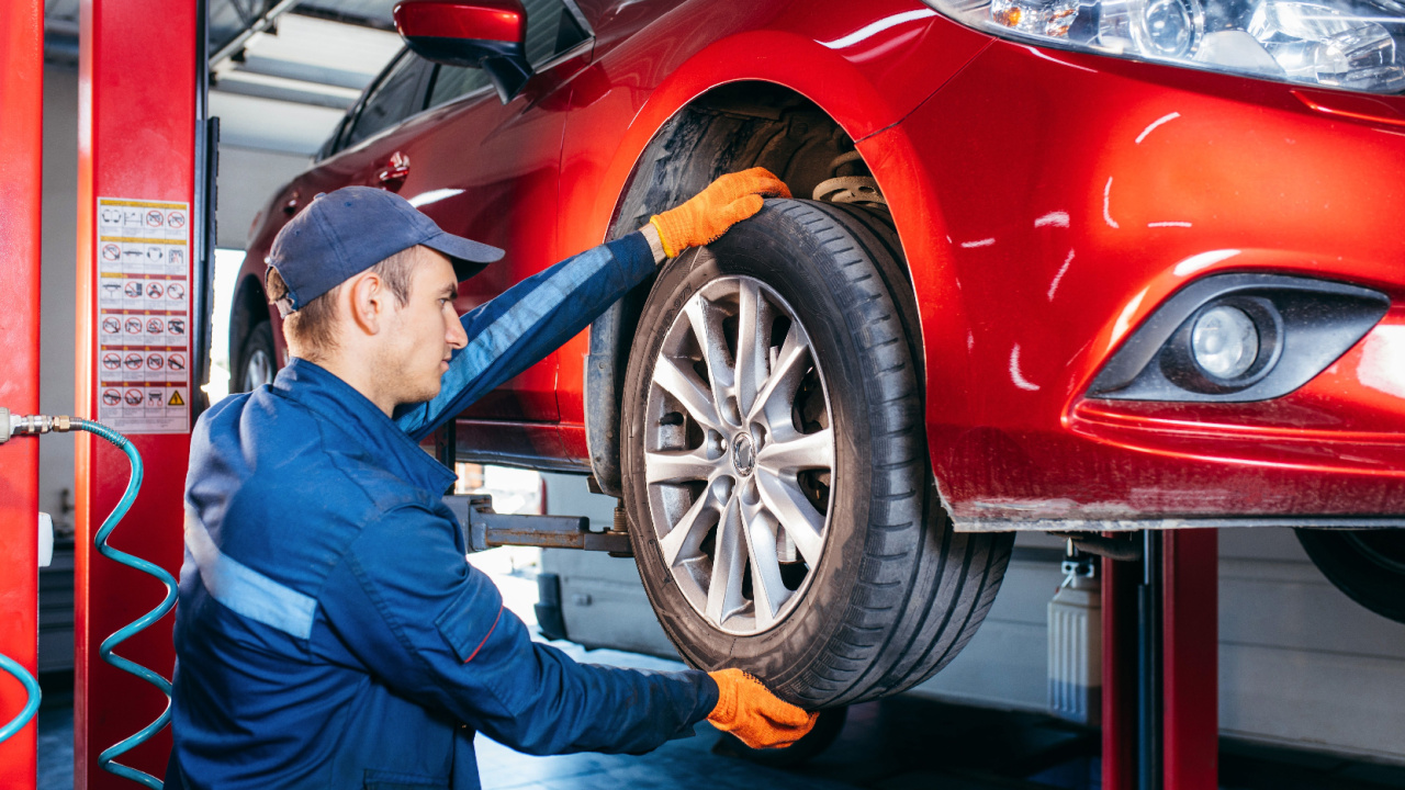 Expert auto specialist technician changes tires, tyres of lifted up car at auto service, wears uniform costume